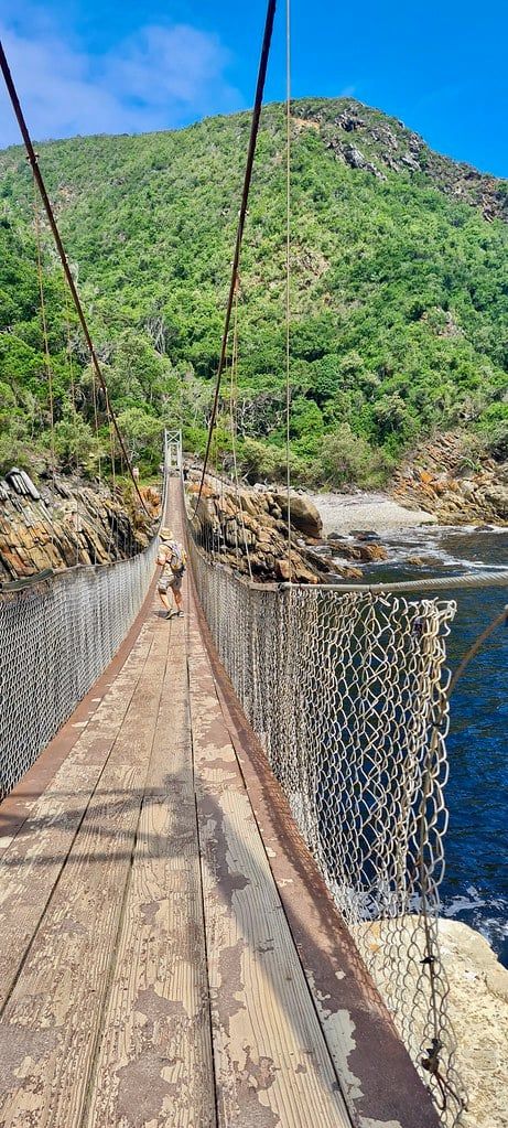 A visitor walks along the wooden suspension bridge over the water at Storms River Mouth in Tsitsikamma National Park along the Garden Route.