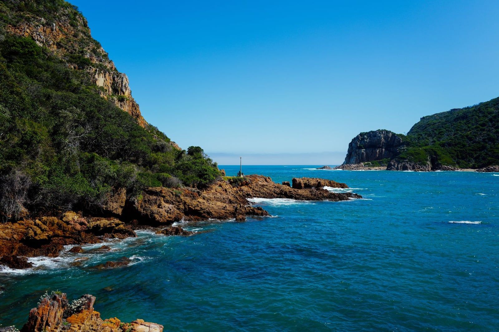 Felsige Sandsteinklippen säumen tiefblaues Küstenwasser an den Knysna Heads an Südafrikas Garden Route.