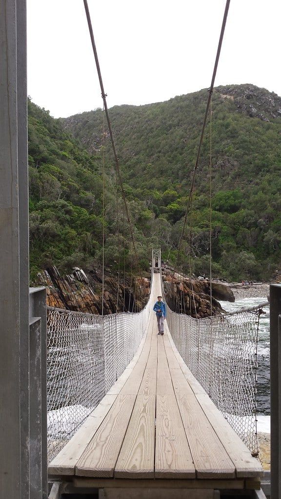 Un visitatore attraversa il ponte sospeso sulla foce dello Storms River nel Parco Nazionale Tsitsikamma, lungo la Garden Route.
