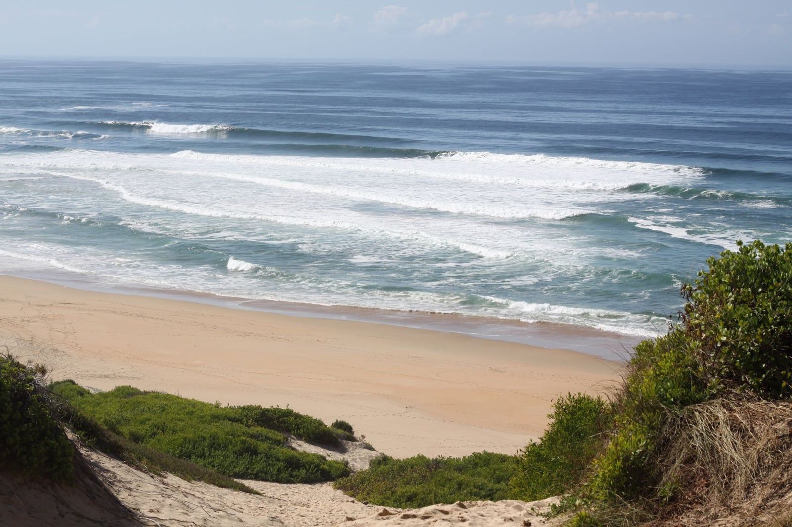 Küstendünen und grüne Büsche blicken auf den Sandstrand und die rollende Brandung in Wilderness an der Garden Route.