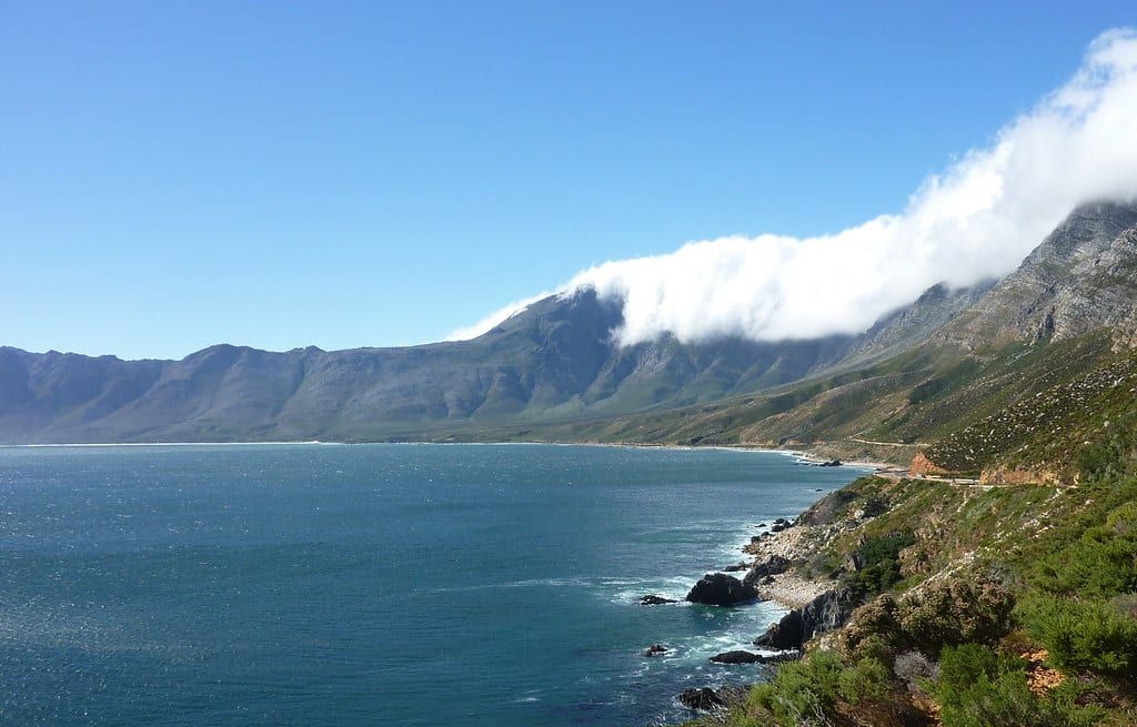 Rugged mountains with low clouds cascading over the peaks meet the ocean along the scenic Garden Route coastline.